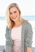 A blonde woman wearing a pink dress and grey cardigan on the beach