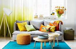 Farbenfrohes Wohnzimmer mit türkisblauem Teppich, grauer Polstercouch und gelben, orangefarbenen Kissen