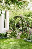 Round arch with climbing roses on the corner of the house in the garden