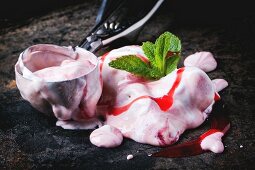 Close up of melting strawberry ice cream with fresh mint and metal spoon over black table