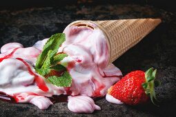 Wafer cone with strawberry ice cream with fresh strawberries and mint over black table