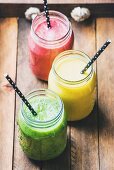 Fresh blended smoothies in glass jars with straws on wooden baclground