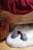 Graue Filzpantoffeln auf weißem Schaffell vor rustikalem Holzbett