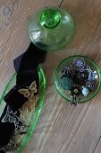 Glass-bead jewellery in green glass pot and decorated black ribbons in glass dish