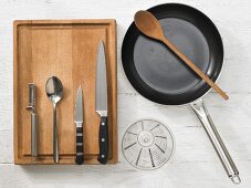 Various kitchen utensils: pan, spoon, measuring cup, peeler, knives
