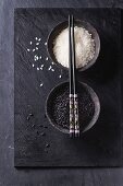 Black and white rice in old metal china bowls with black chopsticks over black slate background