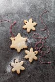 Four snowflake shaped biscuits with a sprinkling of icing sugar in the process of being threaded with red and white bakers twine on a grey slate background