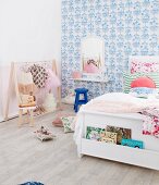 White bed with bookcase in front of blue and white pattern wallpaper and clothes rack with ballet clothes in the girls' room