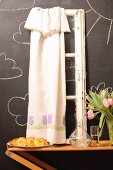 Pastries, carafe, vase of tulips and vintage window frame with curtain against chalkboard wall