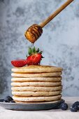 Pancakes with fresh strawberries and blueberries and flowing honey from wooden honey dipper