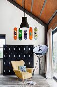 Schwarzer Schliessfachschrank aus Metall, darüber bunte Skateboards an der Wand, gelber Sessel und Fotolampe vor Terrassentür
