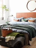Masculine bedroom with leather headboard, blue checked sheets, green throw and round, leather mirror