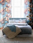 Pastel bed linen and blankets on double bed in front of curtains with pattern of angels