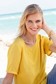 A blonde woman wearing a yellow T-shirt and jeans on the beach