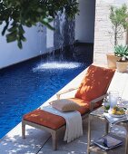 Lounger on summery terrace next to swimming pool with waterfall