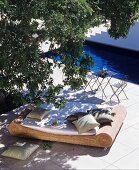 Wicker lounger below tree next to swimming pool