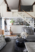 Offener Wohnraum mit grauer Polstergarnitur, im Hintergrund Treppe und Küche