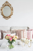 Spherical vase of roses and candelabra on coffee table and gilt-framed mirror above sofa with scatter cushions in background