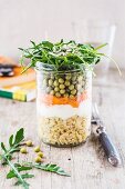A layered salad with rocket, peas, grated carrot and soft wheat in a glass