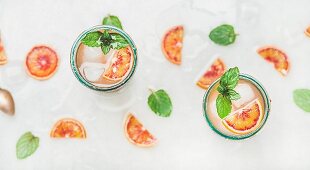 Blood orange fresh summer lemonade with ice and mint in glasses, light grey marble background