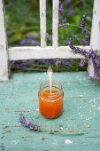 Ein Glas Aprikosenmarmelade mit Lavendelblüten auf altem Holzstuhl