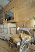 Armchair made from antlers and fur next to chest of drawers against wooden wall