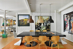 Black dining table and classic chairs in front of white-painted brick wall in open-plan living area