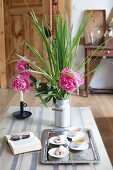 Pastries and tea on tray next to book and pink peonies on table