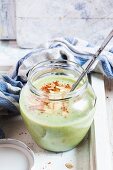Spinach cream soup in a glass jar with roasted almonds and chilli flakes