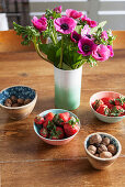 Vase of pink anemones and bowls of strawberries and nuts
