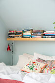 Books on shelf above bed under sloping ceiling