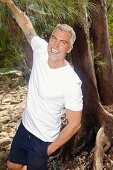 A man with grey hair wearing a white T-shirt and dark blue shorts in the forest