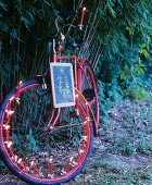Red bicycle decorated with Christmas-tree candles and school slate in front of bamboo