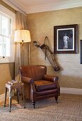 Brown leather armchair and standard lamp below vintage photo and golf bag in corner