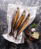 Three smoked mackerels on paper with salt and buttered bread