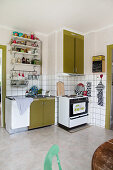 Retro kitchen with olive-green cabinets, old cooker and wall-mounted shelves