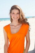 Dunkelblonde Frau in orangefarbenem Kleid am Strand