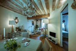 Rustic wood-beamed ceiling, chandelier and antique furniture in open-plan interior of restored period building