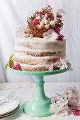 A naked sponge cake decorated with an Easter nest, chocolate eggs, and blossoms