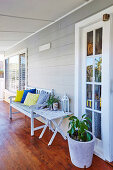 Wooden bench with colorful pillows, side table and potted plant on the veranda