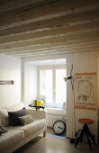 Pale sofa with scatter cushions next to window in period apartment with wood-beamed ceiling