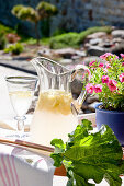Carafe and glass of lemonade next to rhubarb leaf on table