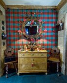 Old chest of drawers and wooden chairs against tartan wall in chalet
