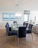 Blue upholstered chairs around dining table in front of seascape paintings on wall in open-plan interior