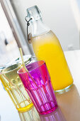 Pink and yellow drinking glasses in front of bottle of pop