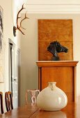 Ceramic pot on exotic-wood table in front of bust of horse and hunting trophy