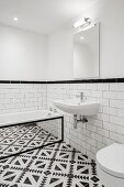 Black and white floor tiles and bathtub with mirrored side in bathroom