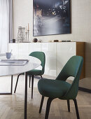 Chairs upholstered in dark green at dining table in front of sideboard with glossy white front