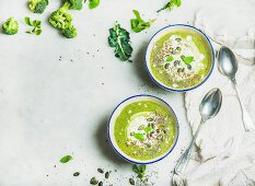 Spring broccoli green cream soup with mint and coconut cream in bowls over light grey marble background