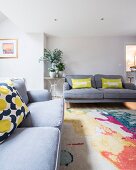 Wohnzimmer mit grauen Sofas und buntem Teppich und Kissen